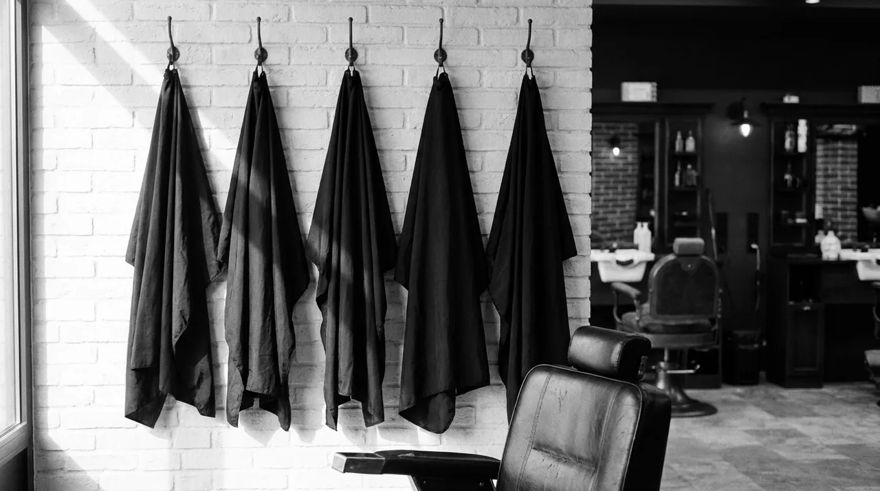 Cinq capes de coupe noires suspendues à des patères sur un mur de briques