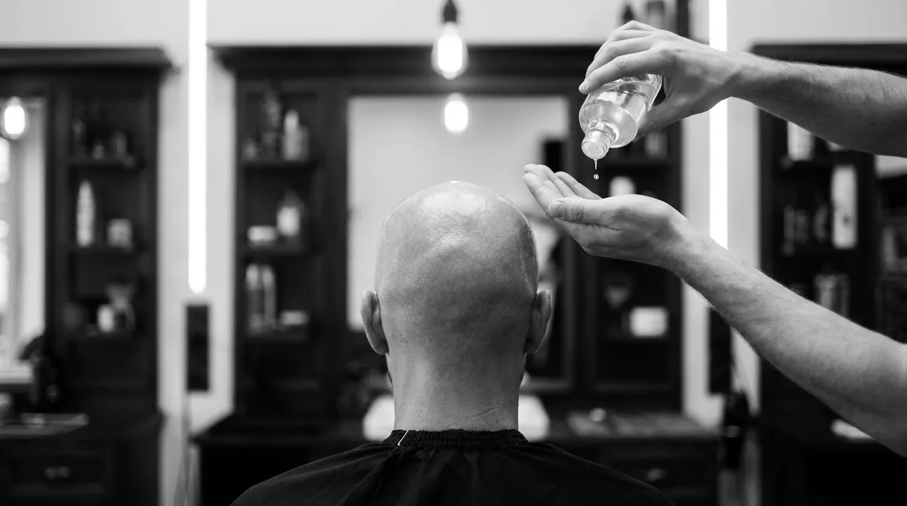 Mains versant quelques gouttes de lotion au-dessus d'un crâne entièrement rasé, vu de dos