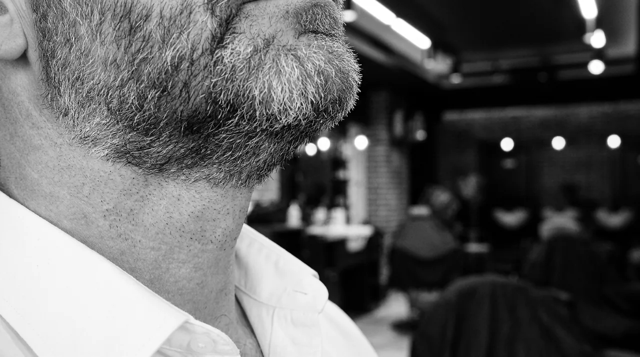 Ligne de barbe poivre et sel nette au-dessus d'un col de chemise blanc ouvert
