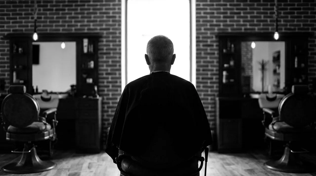 Homme assis dans un fauteuil de barbier, vu de dos à contre-jour devant une vitrine