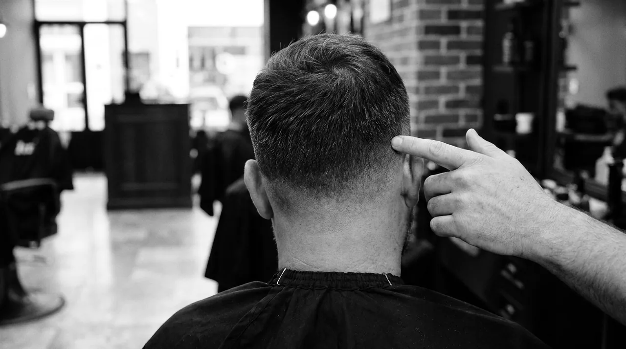 Main d'un barbier posée sur le côté d'un crâne dégradé court, vue de dos