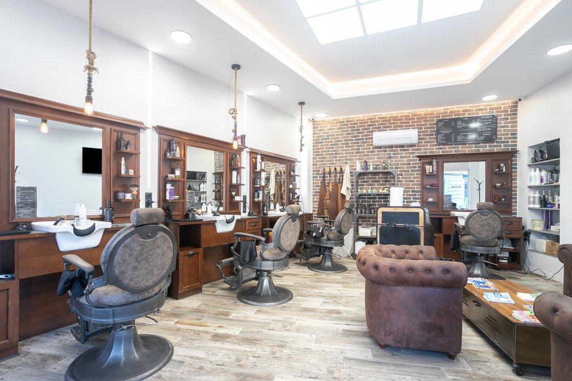 Intérieur du salon Lui Coiffeur à Draguignan : fauteuils de barbier vintage, fauteuil club en cuir et mur de briques sous une verrière