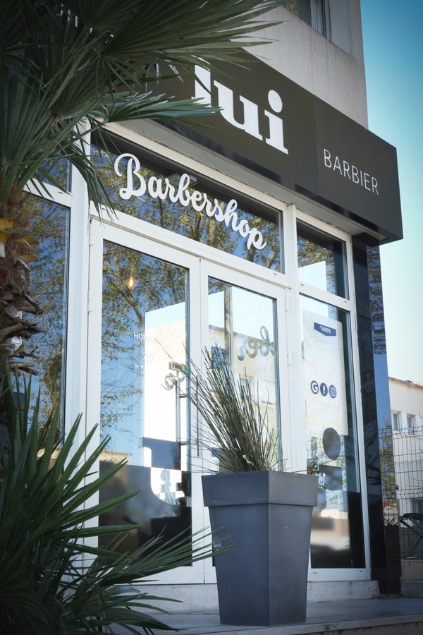 Devanture du salon Lui Coiffeur de Fréjus, vitrine « Barbershop » et palmiers