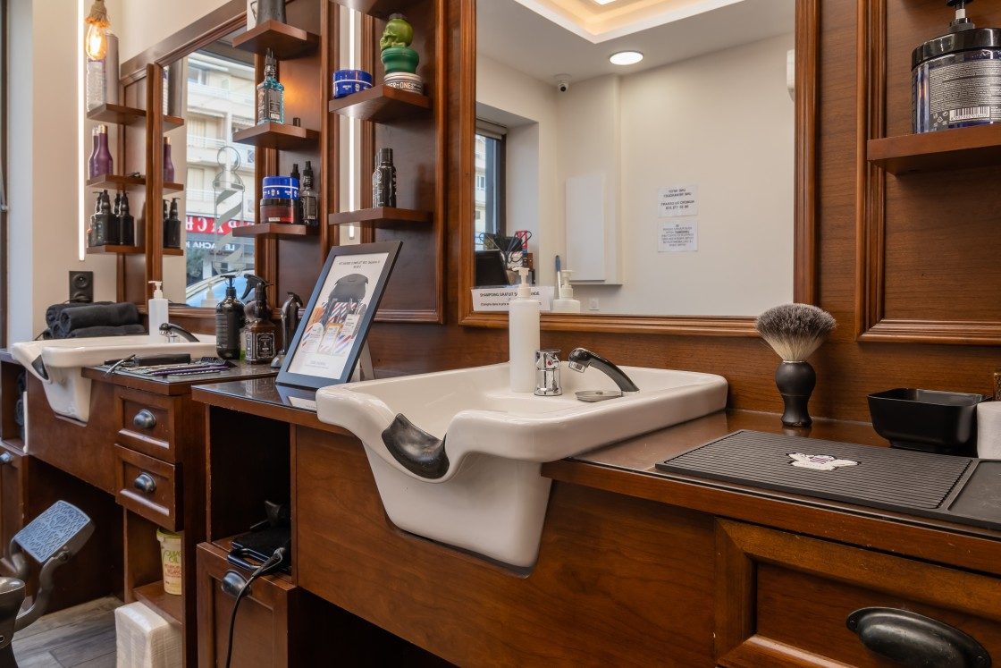 Bac de lavage en porcelaine et coiffeuse en bois avec blaireau et produits au salon Lui Coiffeur à Sainte-Maxime
